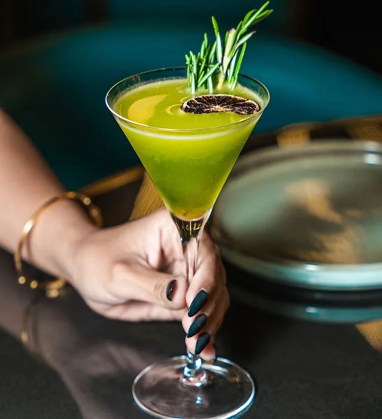 A bright green cocktail garnished with rosemary and dried citrus